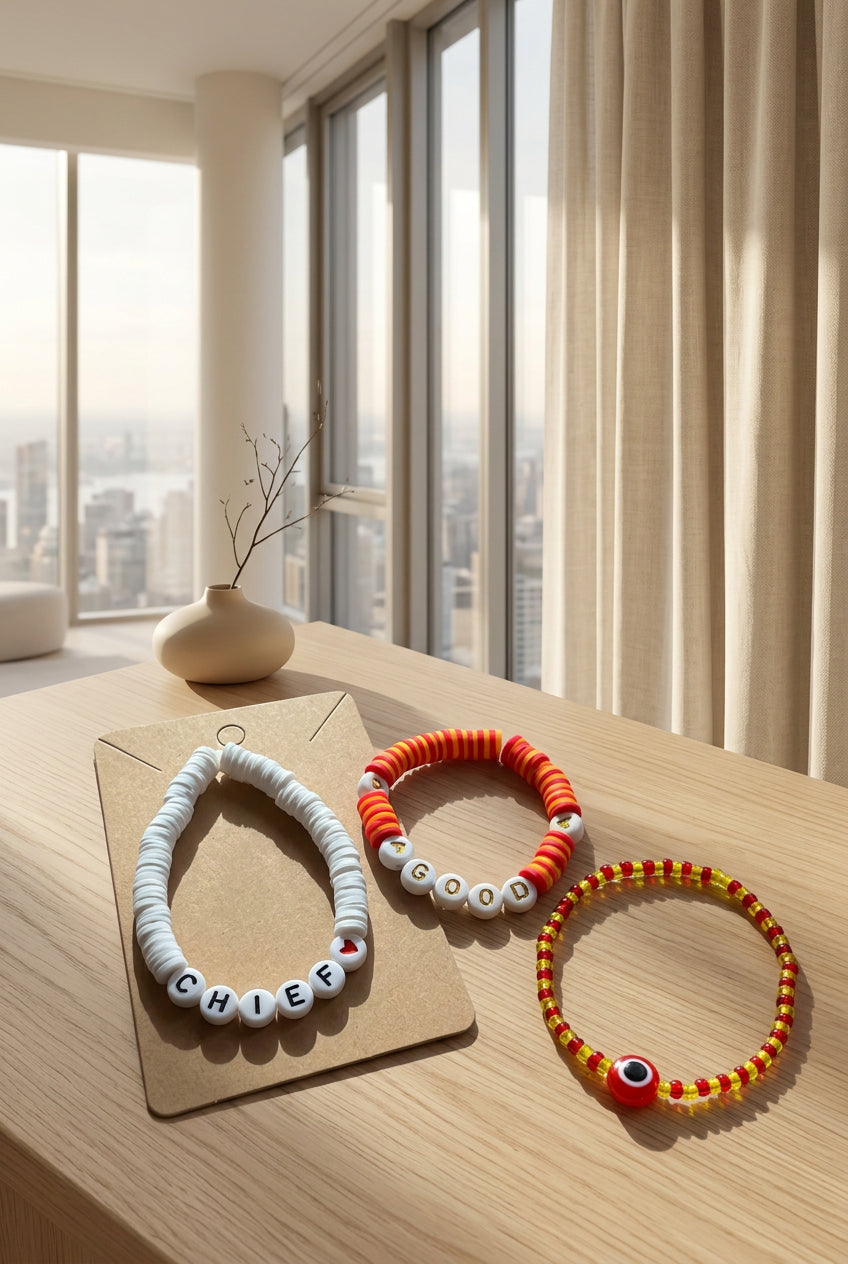 Three handmade beaded bracelets displayed on a kraft paper card against a textured beige fabric background. The bracelets include red and yellow evil eye beads, orange and white letter beads spelling 'LOVE', and white letter beads spelling 'CHIEF' with a small red heart.